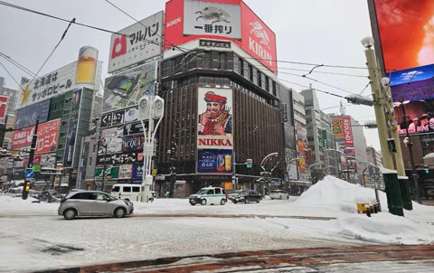 Snowy street scene showing a car driving past a building with many advertisements.