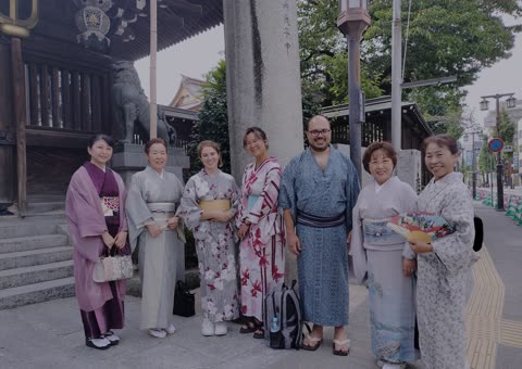 Seven people in kimonos pose outside a Japanese temple.