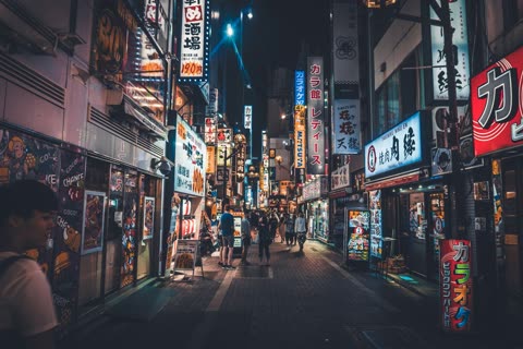 People standing on a brightly lit, narrow Japanese street at night.