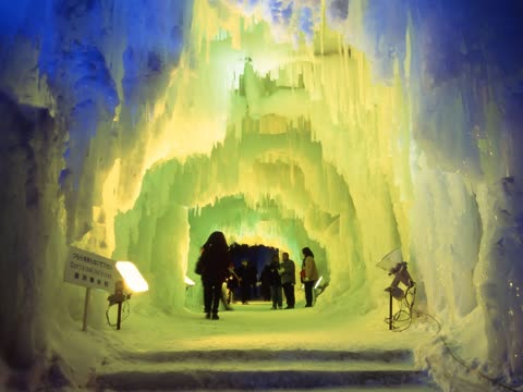 People walk through a lit ice tunnel.