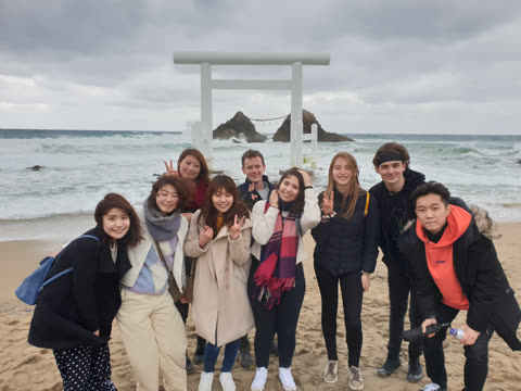 Group posing on beach near a white torii gate.