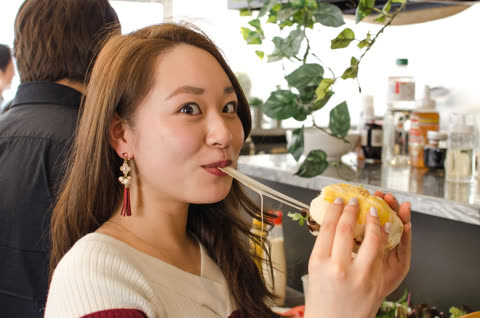 Woman eating burger indoors, cheese stretching.