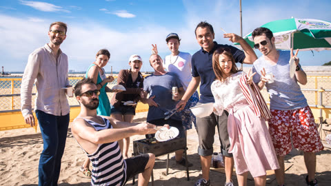 Person grilling food on a beach with a group of people.