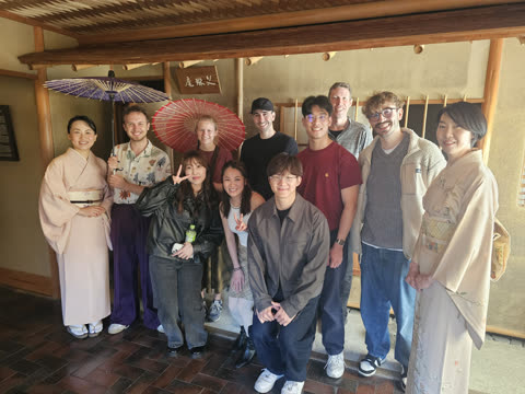 A group of people, including two women in kimonos, pose for a photo inside a traditional Japanese building.