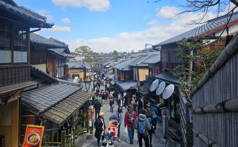 People walking up a narrow street lined with traditional Japanese buildings.