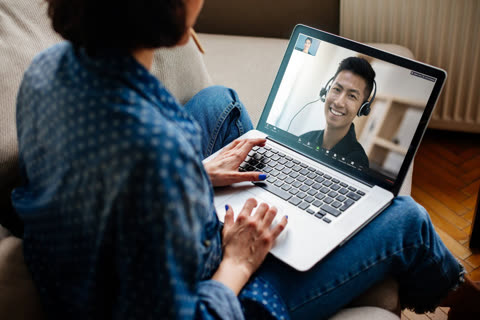 Woman types on laptop, video conferencing with man wearing headset.