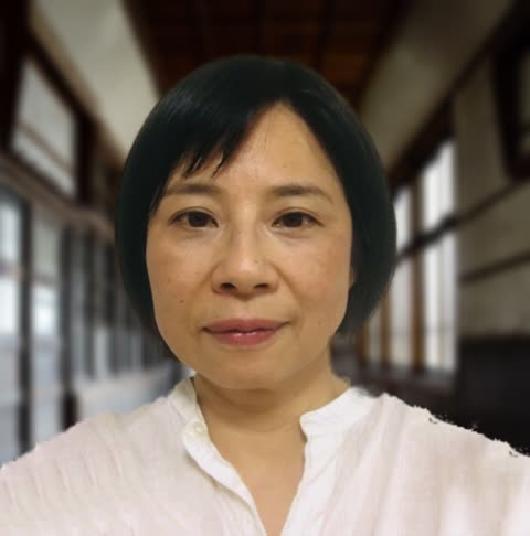 An East Asian woman with short, dark hair and a white collared shirt looks forward inside a blurred hallway.