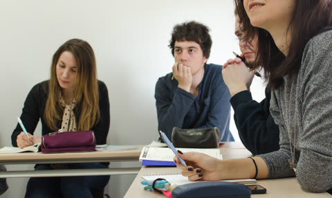Woman writing in notebook at classroom desk.